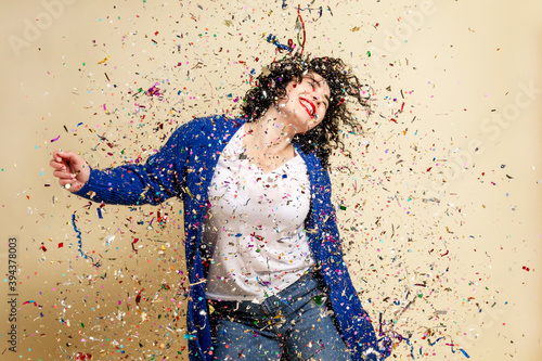 Laughing young brunette girl sprinkled with confetti. Festive mood. New Year's and Christmas. Yellow background.