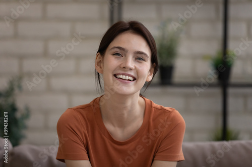Head shot portrait of smiling millennial european woman resting on sofa at home, web camera view happy young lady enjoying online video call conversation with friends, entertaining alone indoors.