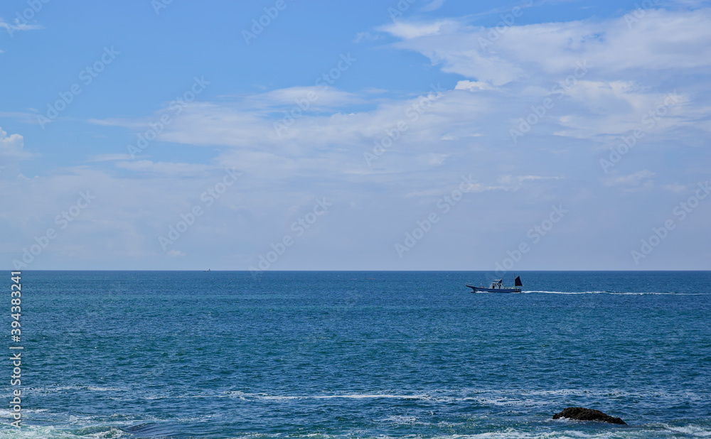 View of the ocean and a distant motorboat moving just under the line of the horizon on a partly cloudy day in late summer