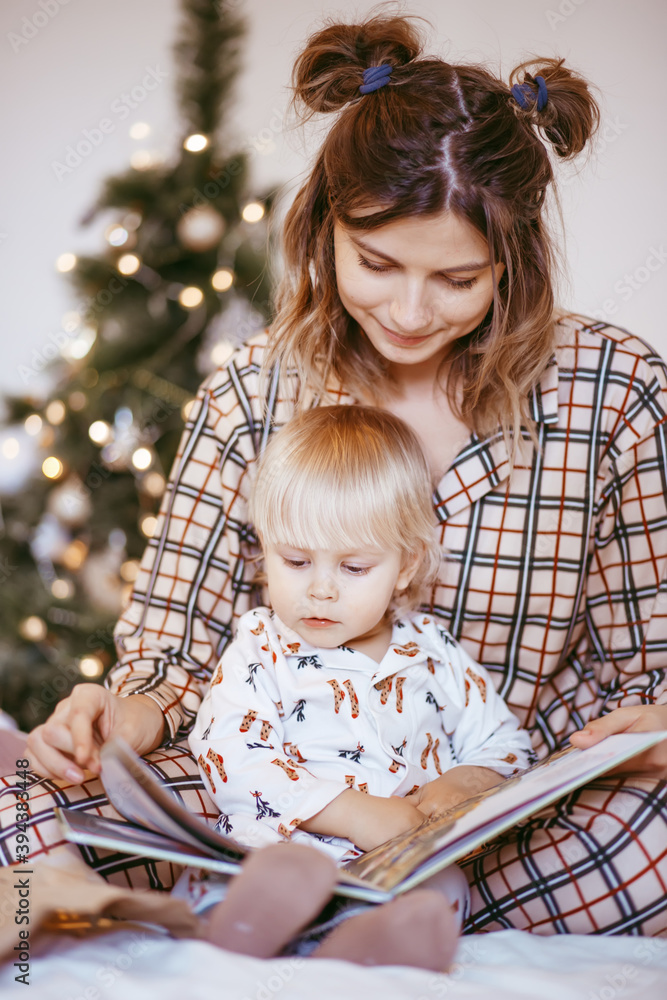Portrait of a happy mother and a charming child at Christmas in a bright interior reading a book together Portrait of a happy mother and a charming child at Christmas in a bright interior reading a book together