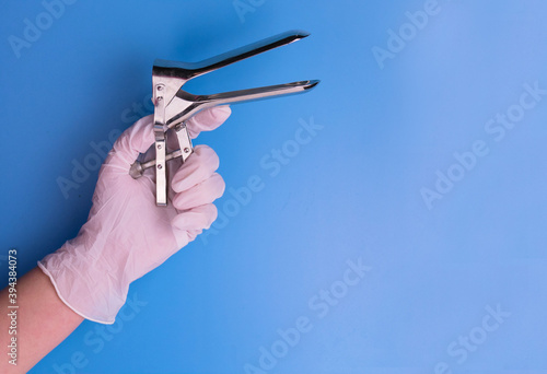 Gynecological mirror in the hand of a doctor on a blue background. Medical tool. 