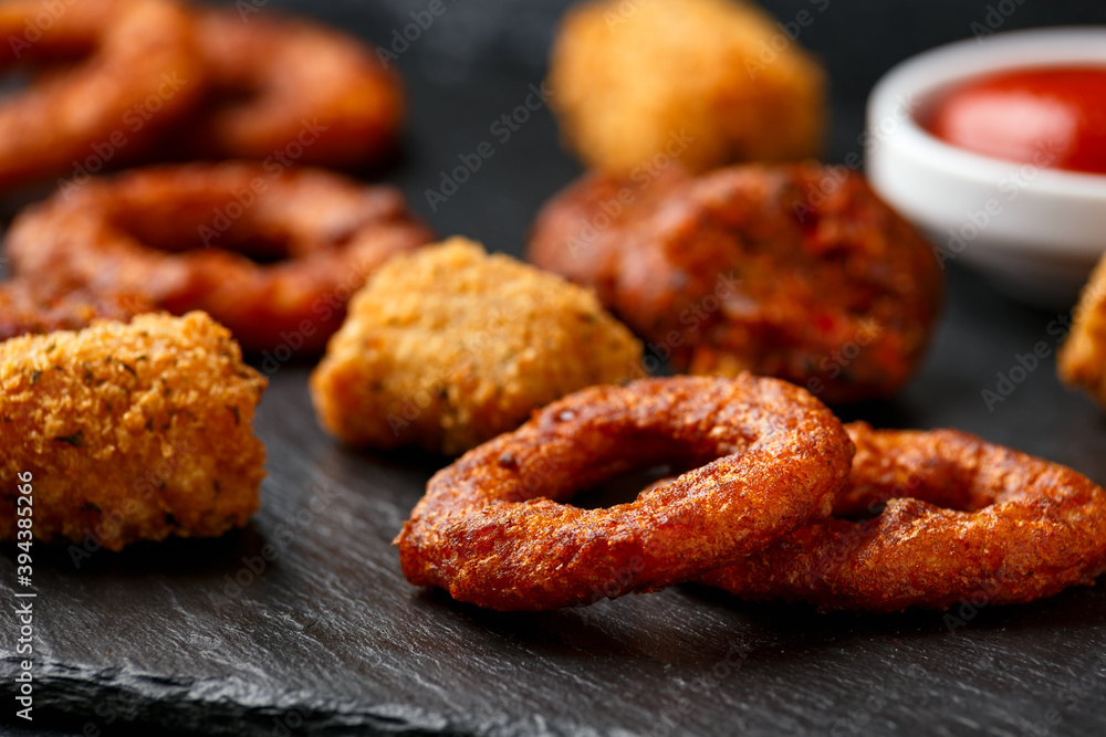 Fried Buffalo onion rings, tater tots and sweetcorn fritters with ketchup on rustic stone board. Party take away food Fried Buffalo onion rings, tater tots and sweetcorn fritters with ketchup on rustic stone board. Party take away food