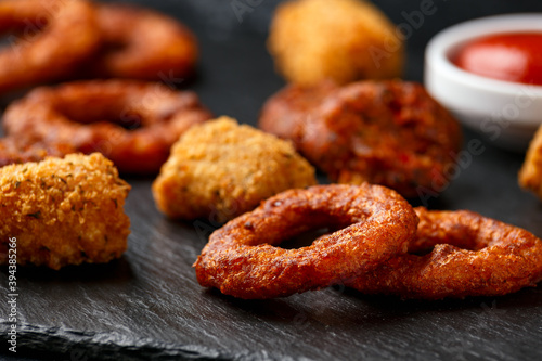 Fried Buffalo onion rings, tater tots and sweetcorn fritters with ketchup on rustic stone board. Party take away food © grinchh