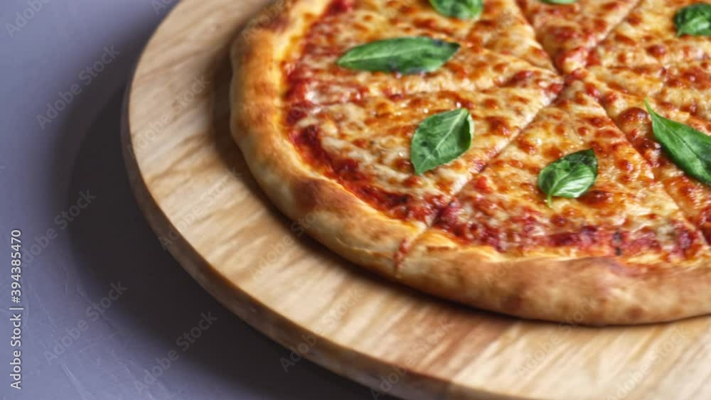 Cheese pizza with basil leaves rotating continually on a wooden plate on white table detail Cheese pizza with basil leaves rotating continually on a wooden plate on white table detail