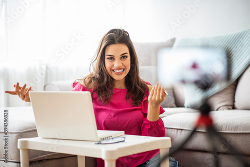 Happy girl at home speaking in front of camera for vlog. Young woman working as blogger  recording video tutorial for Internet. Young female blogger with laptop recording video at home
