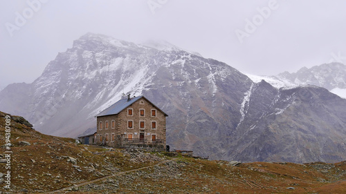 Beautiful view of refuge "Hintergrathütte" in front of snow-covered mountains disappearing in the clouds in the east of Ortler massif near Sulden, South Tyrol, Alps, Italy in autumn season.