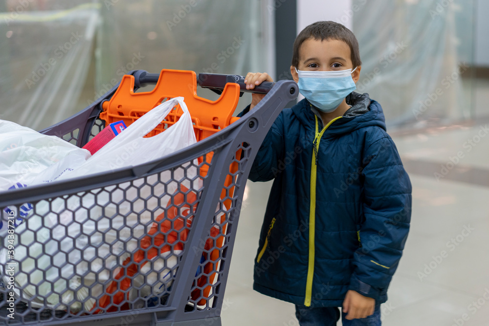 Fototapeta premium Boy wears protected mask in store. Shopping time during coronavirus outbreak. Boy in a medical mask. Shopping with kids during virus outbreak. Boy in face mask in supermarket