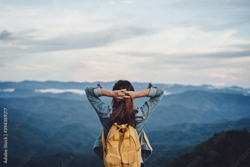 Happy young woman traveler relaxing and looking at the beautiful sunset on the top of mountain Happy young woman traveler relaxing and looking at the beautiful sunset on the top of mountain
