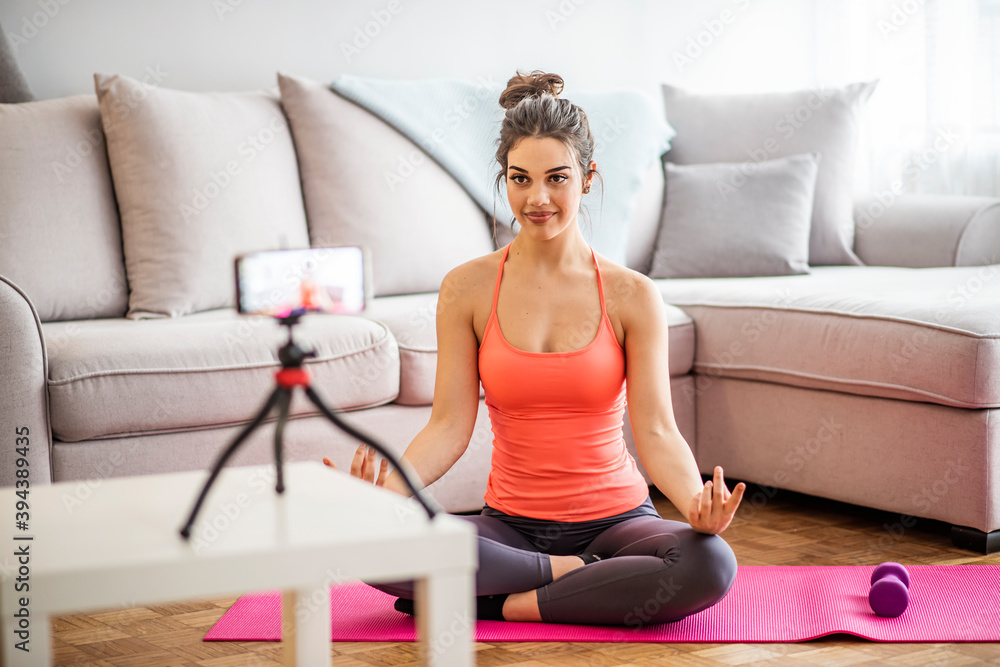 Beautiful young woman doing a streaming session of her doing yoga in her apartment during corona virus quarantine. Portrait of a beautiful young yoga instructor recording a video for her blog at home Beautiful young woman doing a streaming session of her doing yoga in her apartment during corona virus quarantine. Portrait of a beautiful young yoga instructor recording a video for her blog at home