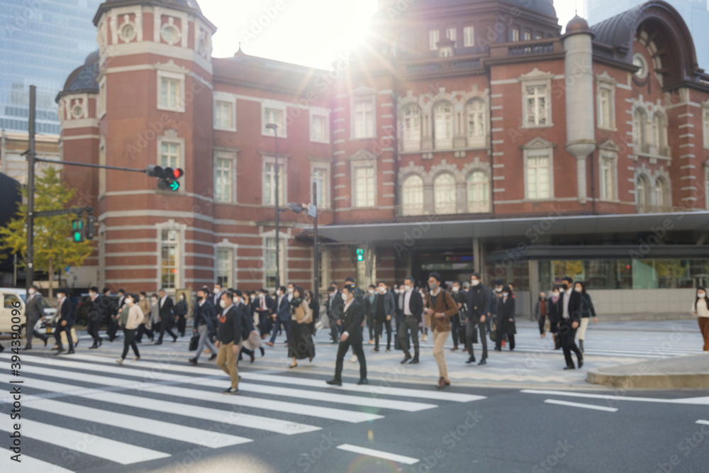 意図的にピントをぼかした東京駅前の横断歩道を渡るマスク姿のビジネスマンたち