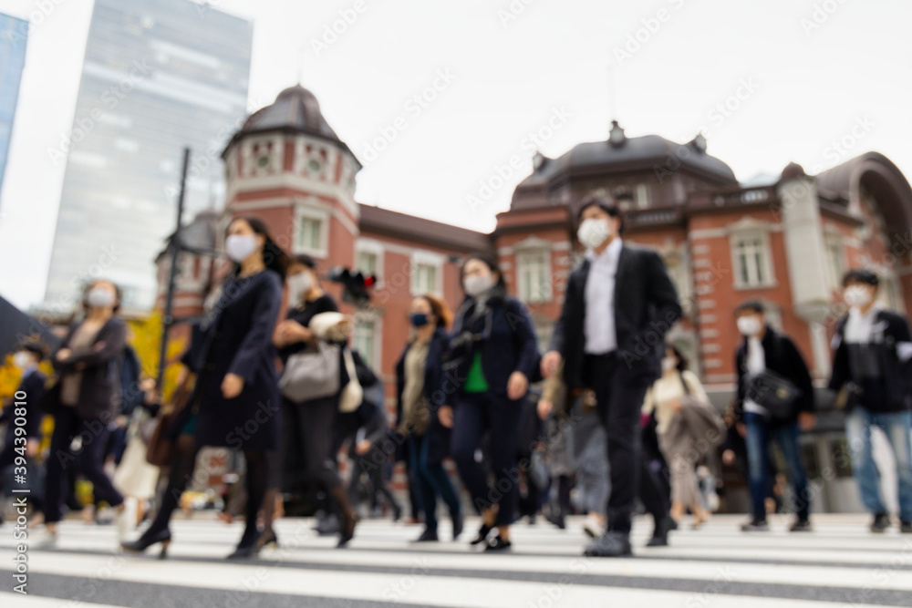 意図的にピントをぼかした東京駅前の横断歩道を渡るマスク姿のビジネスマンたち