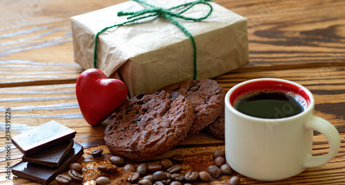 image of a cup with coffee, pieces of chocolate, coffee beans, chocolate chip cookies, stylized red heart and a holiday gift box