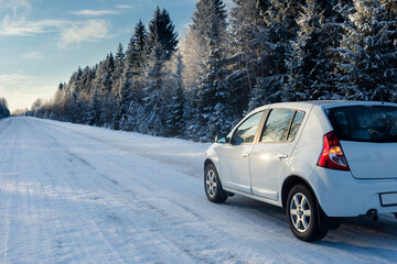 White car on a winter road through a snow covered forest.	
