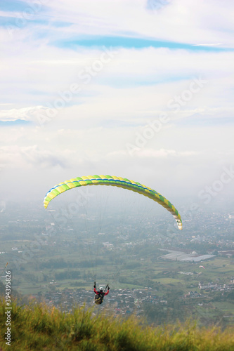 Paragliding in a cloudy sky with city views and a green yellow parachute
