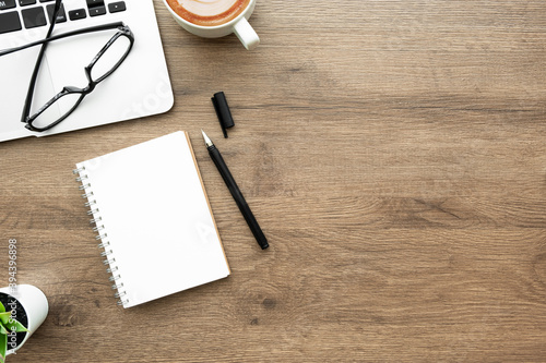 Blank notebook with pen are on top of wood office desk table with laptop computer, cup of coffee and suplpies. Top view with copy space. Morning life working from home concept.