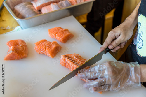 Chef use knife preparing a fresh salmon on a cutting board, Japanese chef in restaurant slicing raw salmon, ingredient for seafood dish. Chef with a knife cutting raw salmon.
