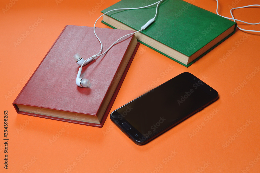 book, smartphone, headphones on an orange background. audiobook. hobby. free time. recreation. literature. book, smartphone, headphones on an orange background. audiobook. hobby. free time. recreation. literature.