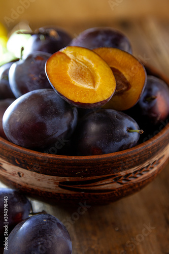 Blue plum in a bowl on a wooden table. Plums in a cut. Top view, place for text. Fruit background with copy space. Still life food.