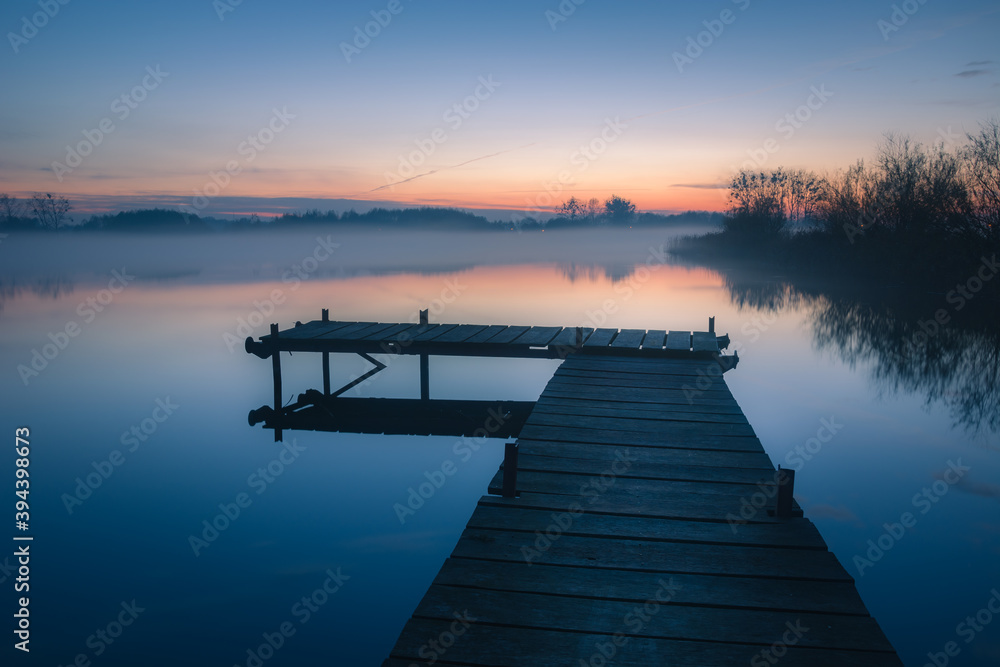 Naklejka premium Wooden platform on a calm lake after sunset