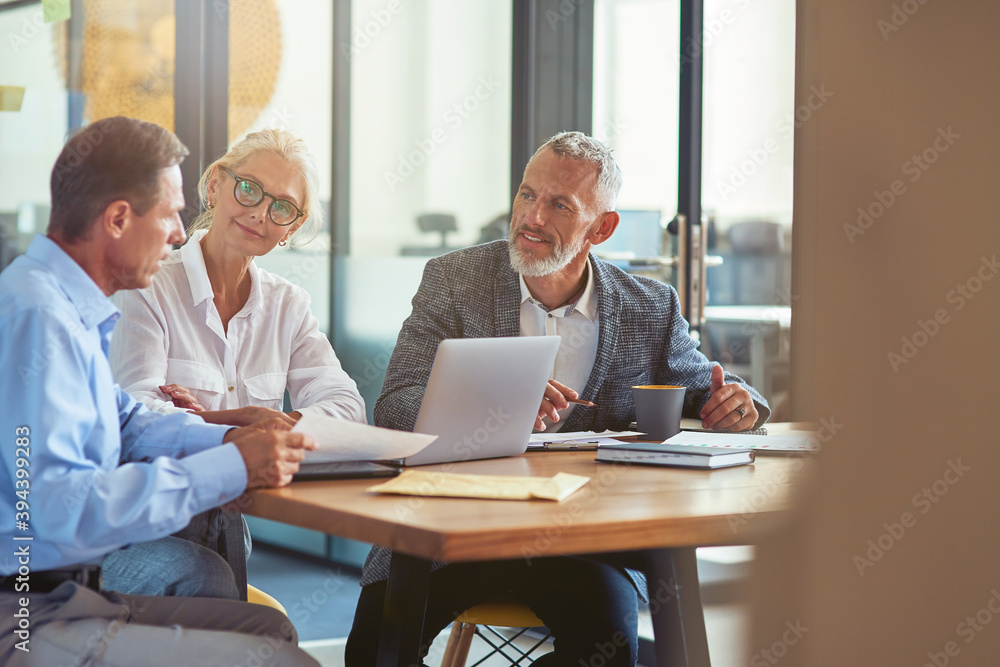 © Kostiantyn - Three mature colleagues sitting in the modern office and discussing business strategy, business people working together