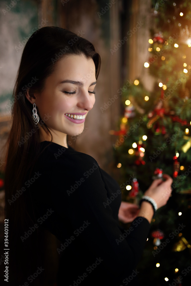 young girl in a festive mood in a black dress by the Christmas tree