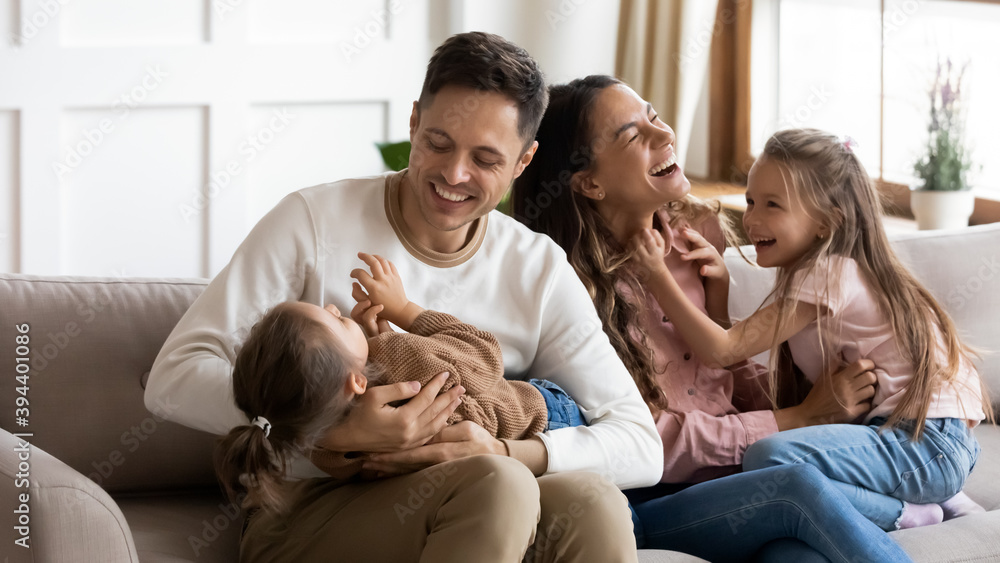 Funny parents play with two daughters resting on couch in light cozy living room. Family enjoy playtime together at home, tickling each other laughing feels happy. Having fun at home with kids concept Funny parents play with two daughters resting on couch in light cozy living room. Family enjoy playtime together at home, tickling each other laughing feels happy. Having fun at home with kids concept