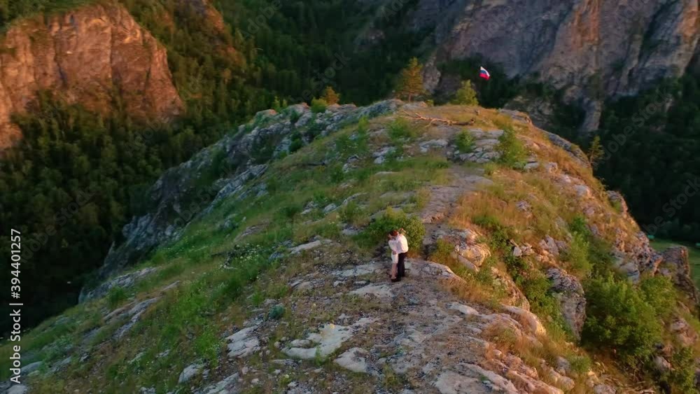 A couple in love at sunset kissing on a mountain with a Russian flag aerial video filming flying around the camera A couple in love at sunset kissing on a mountain with a Russian flag aerial video filming flying around the camera
