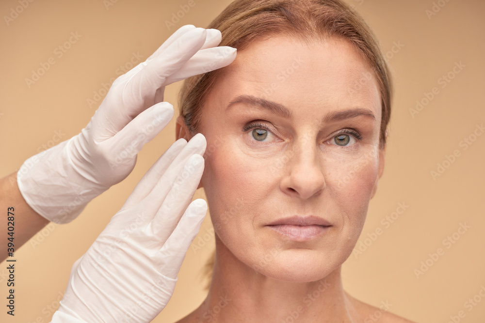 Plastic surgery concept. Beautician hands in white gloves checking female face skin before medical therapy Plastic surgery concept. Beautician hands in white gloves checking female face skin before medical therapy