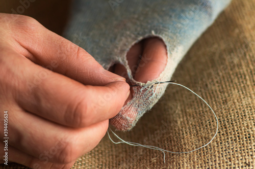 Hands sew up the hole in the sock.