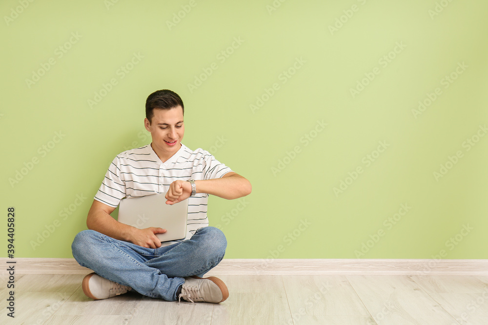 Young man with wristwatch and laptop sitting near color wall Young man with wristwatch and laptop sitting near color wall