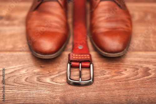 Classic men's brown leather shoes with a belt on a wooden background.
