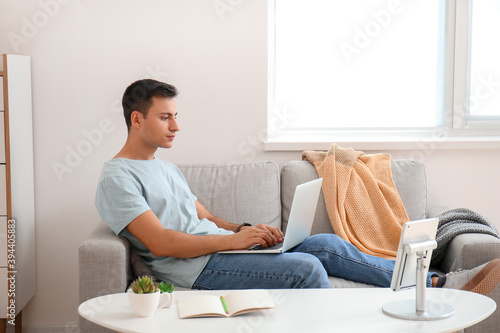 Young man working remotely on laptop from home sofa, modern lifestyle and dig...