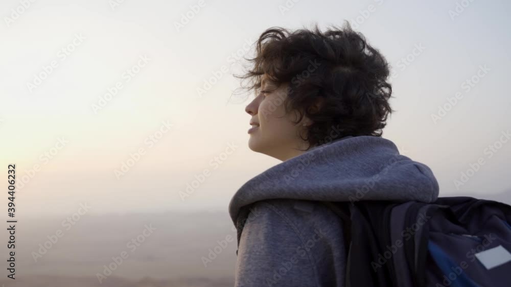 Young woman traveling in desert smiles, takes deep breathe when reaching summit. Backpacker enjoying the view and fresh air in the cold early morning on top of a hill after climbing for hours Young woman traveling in desert smiles, takes deep breathe when reaching summit. Backpacker enjoying the view and fresh air in the cold early morning on top of a hill after climbing for hours