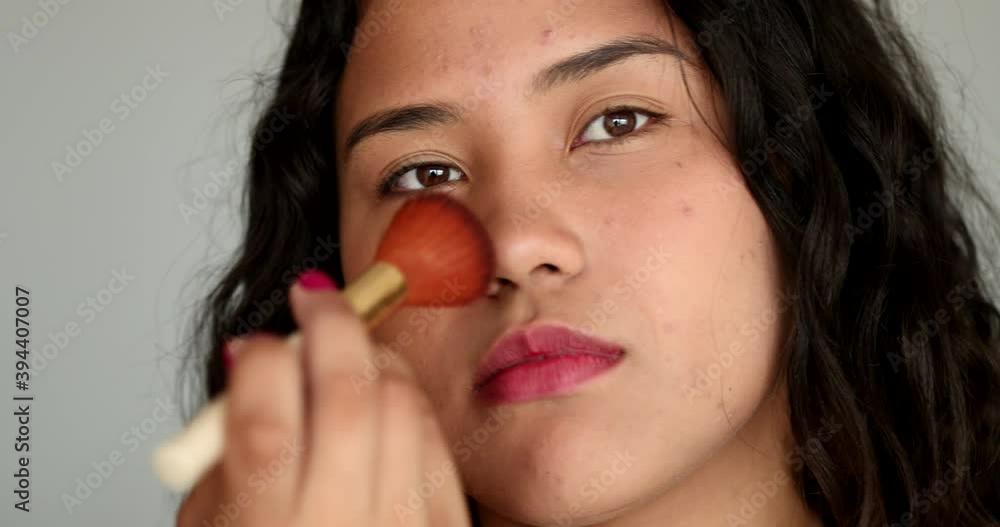 Casual Latina Hispanic woman applying make-up brush, looking at camera Casual Latina Hispanic woman applying make-up brush, looking at camera