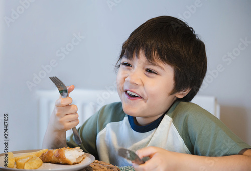 Healthy kid eating fried battered fish fillet for brunch, Happy young boy eaitng fish and chips for his lunch, Child enjoying having homemade sunday unch at home.New normal, healhty life style concept photo