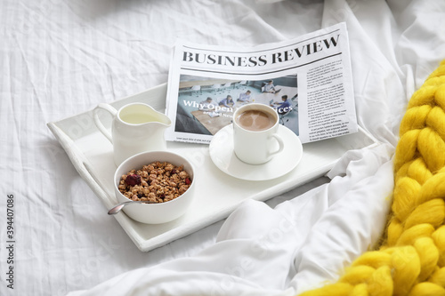 Tray with tasty breakfast and newspaper on bed