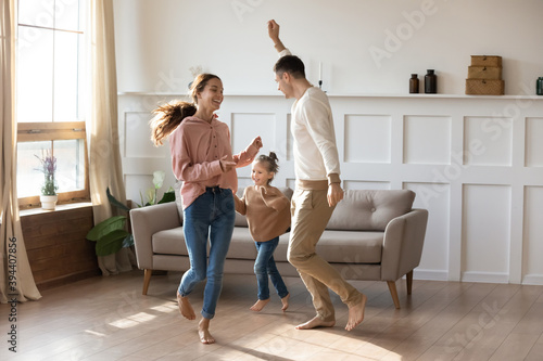 Cheery couple dancing with little daughter barefoot on wooden laminate floor with underfloor heating system in modern warm living room. New home, bank loan and lending, hobby and fun with kids concept photo