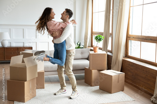 Happy couple arrive at bought house, cheerful husband lifts up on hands beloved wife family begin new life at first dwelling. Loan and mortgage, bank lending, delivered goods satisfied clients concept photo