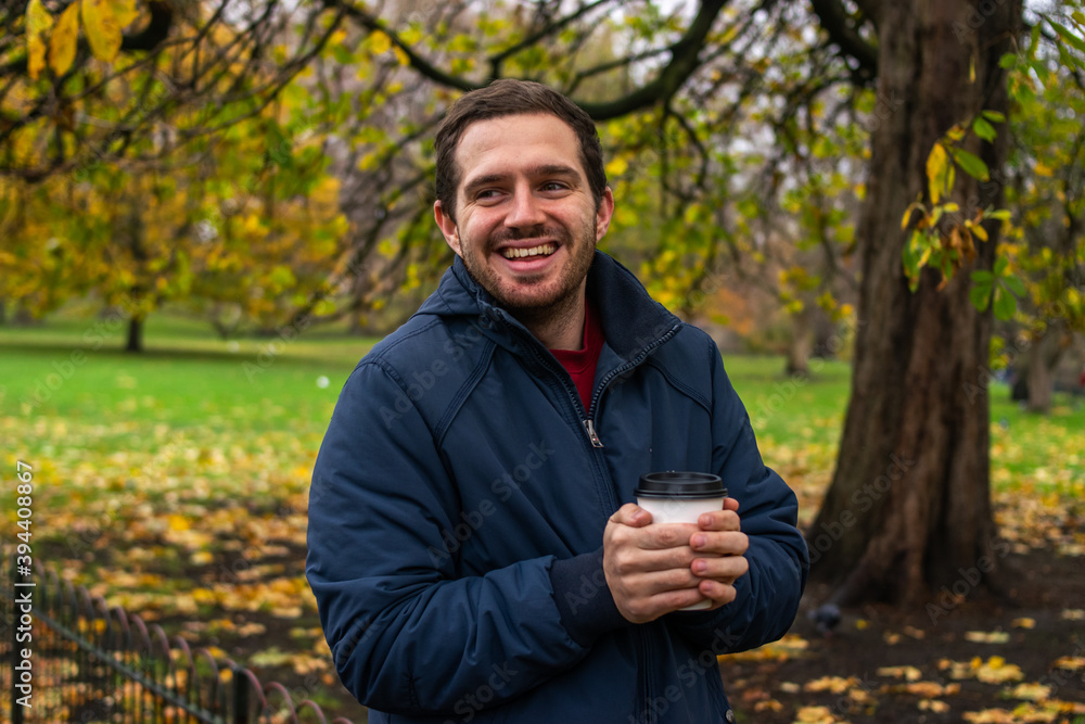 Photo of a young and attractive man enjoying a cup of coffee walking in the park during a day of autumn. Photo of a young and attractive man enjoying a cup of coffee walking in the park during a day of autumn.