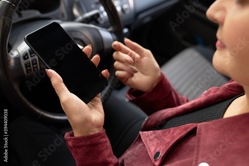 Cropped shot of busy female driving car and typing text message on mobile. Close up image of woman hands holding cell phone while being stuck in traffic, sitting in driver seat. Selective focus