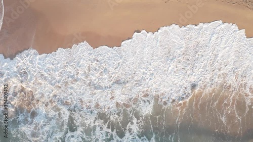 Aerial drone shot of waves crashing on beach at sunrise.