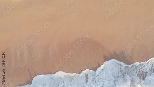 Aerial drone shot of waves crashing on beach at sunrise.