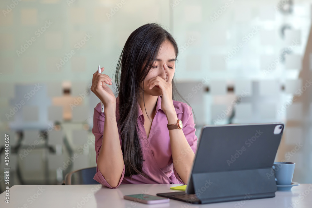 Portrait of a tired young asian businesswoman sitting at the table with laptop computer in office. Portrait of a tired young asian businesswoman sitting at the table with laptop computer in office.