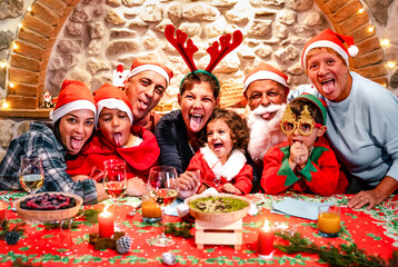 Funny selfie pic of multi generation large family with santa hats having fun at Christmas fest house party - Winter holiday xmas concept with grand parents and children eating together - Vivid filter