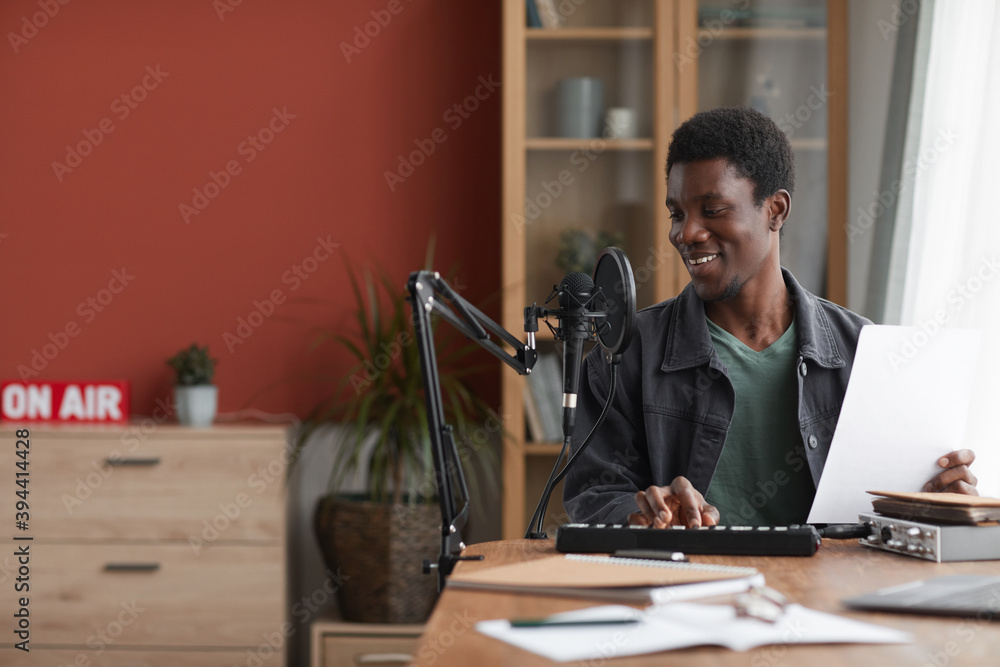 Portrait of smiling African-American man singing to microphone while recording music in home studio, copy space