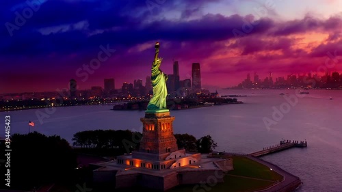 Aerial view around glowing statue of liberty, during a colorful sunset, dark clouds rolling in, in New York, USA - Orbit, drone shot