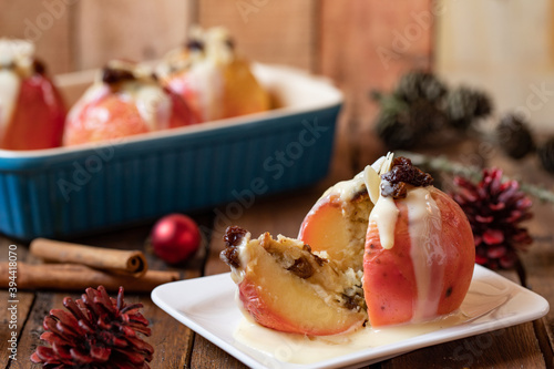 gebackener Bratapfel mit Füllung aus Marzipan, Mandeln, Rosinen und Zimt mit Vanillesoße zur Winterzeit und Weihnachten auf einem braunen Tisch aus Holz in der Küche