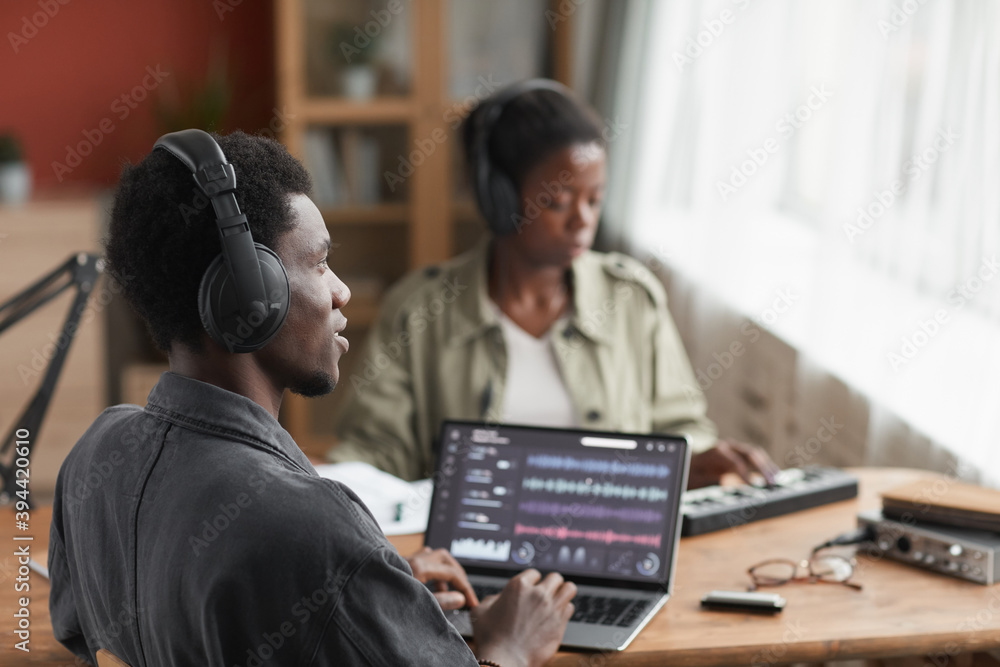 Profile view at young African-American musician wearing headphones while composing music at home recording studio, copy space Profile view at young African-American musician wearing headphones while composing music at home recording studio, copy space