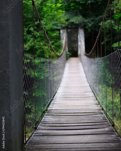 Fototapeta Naklejka Na Ścianę i Meble -  Eine Hängebrücke aus Holz über einen Fluss mit Blick auf die andere Seite, auf der ein Wald zu sehen ist. 