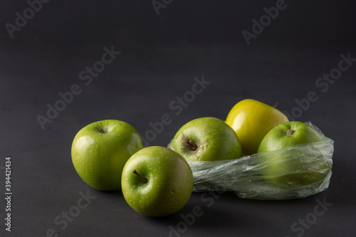 single use plastic packaging issue. green apples in plastic bags  on a dark background